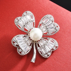 Elegant silver four-leaf flower brooch with zircon stones and center pearl on red surface