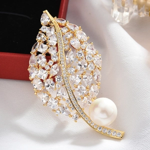 Detail of a leaf brooch with sparkling zircons and a premium white pearl on red velvet
