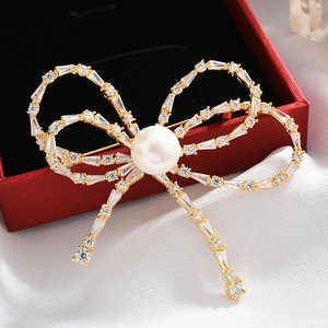 Detailed close-up of a bow-shaped golden brooch with a large pearl and sparkling zircons