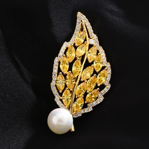 Detailed view of a gold leaf brooch featuring yellow stones and a white pearl on silk