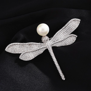 Macro shot of silver dragonfly brooch with white pearl head and cubic zirconia wings
