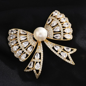 Elegante spilla a fiocco dorata con pietre di zircone e una grande perla bianca centrale