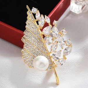 Macro shot of an elegant gold leaf brooch featuring white pearl and zircon crystal details