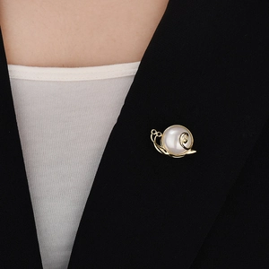 Détail d'une broche escargot dorée avec perle blanche sur le revers d'une veste noire
