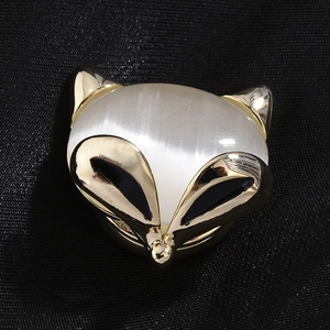 Élégante broche renard dorée avec pierre œil de chat blanche sur un tissu texturé noir chic