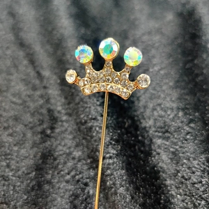 Detail of a gold crown brooch with colorful AB rhinestones and a long lapel stick pin