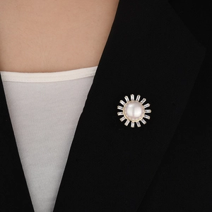 Detail of sunburst shell brooch with white pearl and baguette crystals on black blazer