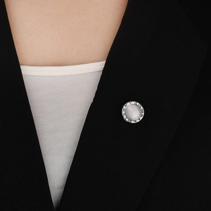Detail of a round Roman numeral brooch with white shell center on black blazer lapel