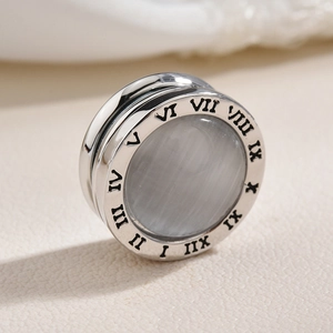 Silver magnetic brooch with Roman numerals and grey cat eye stone on beige background