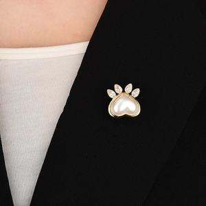 Détail d'une broche patte de chat dorée avec perle de coeur et zircon sur un revers