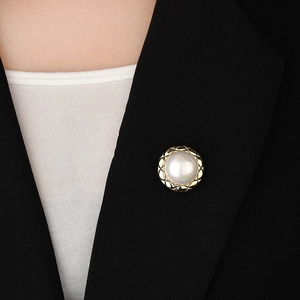 Elegant round pearl brooch with gold quilted texture frame on a black suit lapel