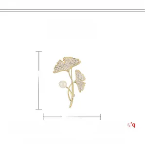 Détail macro d'une broche feuille de ginkgo dorée avec zircone et une perle blanche