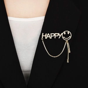 Broche dorée avec lettres HAPPY et visage souriant en zircon sur revers de veste