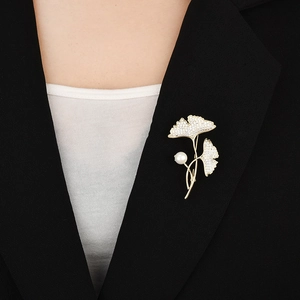 Élégante broche feuille de ginkgo dorée avec perles et cristaux sur un blazer noir