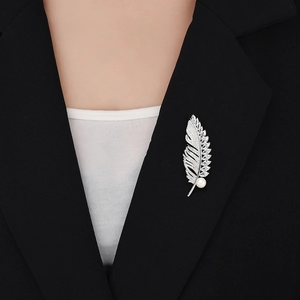 Détail d'une broche plume en zircon et perle portée sur le revers d'un blazer noir
