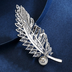 Broche plume argentée avec zircons brillants et perle sur fond bleu élégant
