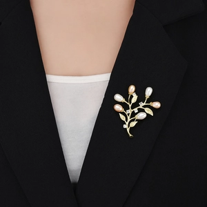 Vue détaillée d'une élégante broche feuille dorée avec perles blanches et roses sur blazer