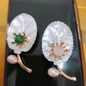 Détail d'une broche florale en nacre avec pierre verte, perle et accents dorés