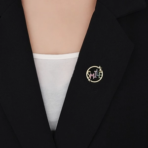Detail einer goldenen SMILE Brosche mit bunten Zirkonsteinen auf einem schwarzen Revers