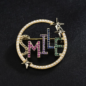 Eleganter goldener SMILE Kreis-Brosche mit bunten Zirkonia und Perlen auf schwarzem Stoff