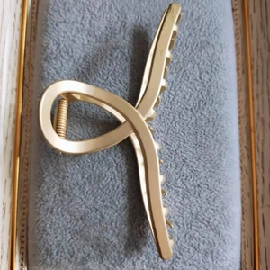 Détail d'une pince à cheveux en métal doré mat avec design croisé sur support en velours