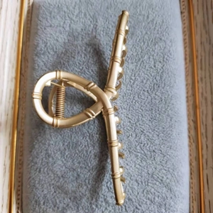 Détail d'une pince à cheveux dorée mate avec texture bambou et structure torsadée