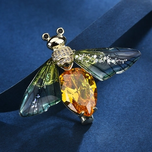 Elegant insect bee brooch with yellow crystal and green translucent wings on blue background