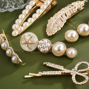 Détail de barrettes dorées en perles avec plumes, étoiles de mer et nœuds strass