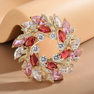Broche couronne de fleurs dorée avec zircons roses et rouges sur présentoir beige chic