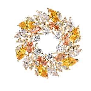Élégante broche en forme de couronne de fleurs dorée avec zircons jaunes et orange sur blanc