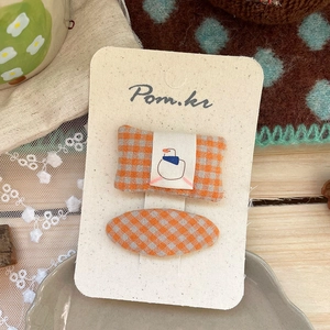 Detail view of handmade orange plaid fabric hair clips set on a Pom.kr display card