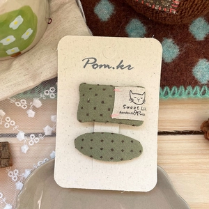 Detail of sweet green polka dot fabric hair clips with handmade cat label on wood surface
