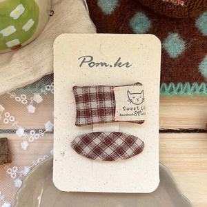Detailed view of two handmade brown plaid fabric hair clips with cat patch on wooden background