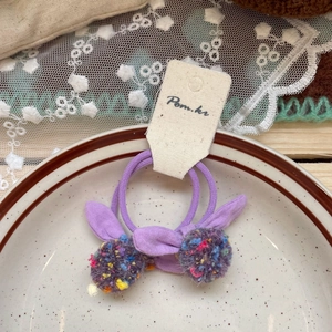 Detail view of two purple rabbit ear hair ties with colorful pom-poms on a white ceramic plate