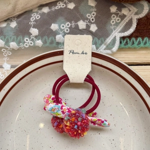 Detail of red floral bow hair ties with colorful pom-poms on a vintage ceramic plate