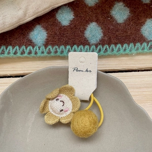 Detail einer gelben Blumen-Haarspange mit Smiley und Bommel auf strukturiertem Stoff