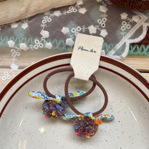 Detail of floral bow hair ties and colorful pom-poms on a rustic ceramic display tray