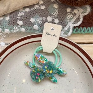 Detail of mint green elastic hair ties with floral rabbit ears and soft pom-poms