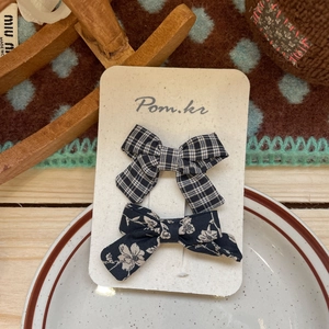 Close-up of two fabric bow hair clips with plaid and floral patterns on display card