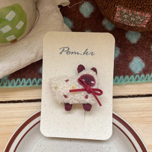 Détail d'une adorable pince à cheveux mouton en peluche beige avec ruban rouge