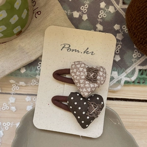 Détail de barrettes en tissu en forme de cœur avec motifs à pois et fleurs sur fond rustique