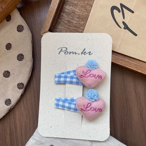 Détail de barrettes artisanales en tissu à carreaux bleus avec cœurs roses brodés Love