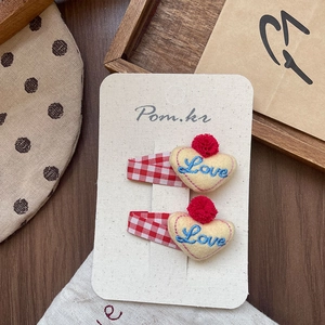 Détail des pinces à cheveux coeur en feutre jaune avec broderie Love et pompons