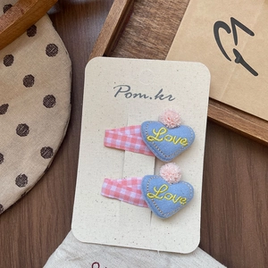 Détail de douces barrettes à cheveux en tissu bleu en forme de cœur avec broderie Love jaune