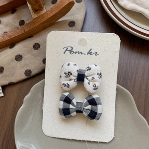 Detailed view of handmade fabric bow hair clips with floral and plaid patterns on card