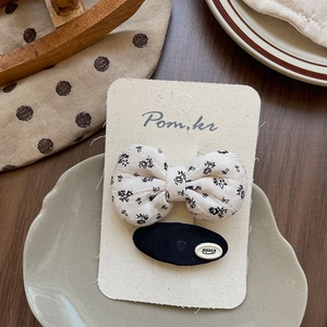 Close-up of a floral bow hair clip and black oval logo clip on a branded display card