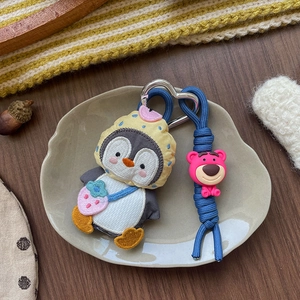 Dettaglio portachiavi pinguino di peluche con felpa gialla a pois e ciondolo orso