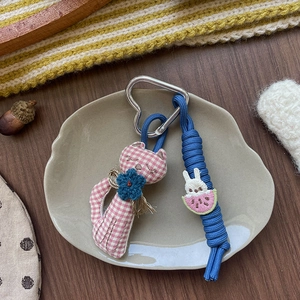 Dettaglio del portachiavi a forma di gatto in tessuto rosa con cordino blu e fibbia a cuore