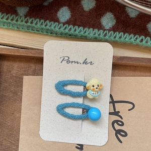 Détail de barrettes en tricot bleu avec petit chien jaune et perle brillante