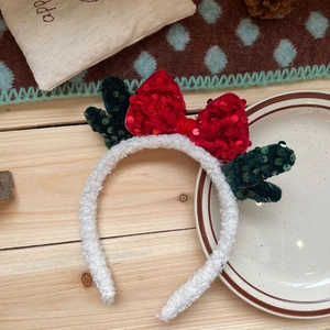 Close-up of a Christmas headband with red sequin bow, green antlers, and white velvet texture